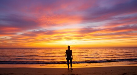 Silhouette of a person standing on a beach at sunset, vibrant colors fill the sky.