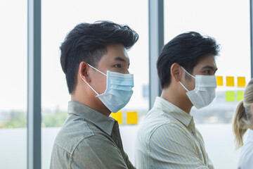 Asian office workers wearing protective face masks inside modern workplace, symbolizing occupational health, corporate safety measures, and adaptation to new normal business environment.