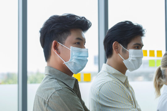 Asian office workers wearing protective face masks inside modern workplace, symbolizing occupational health, corporate safety measures, and adaptation to new normal business environment. - Powered by Adobe