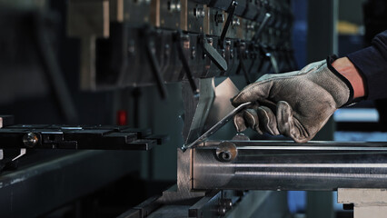 Sheet metal bending on CNC machine. Gloved worker bending a metal sheet using a CNC press brake in...