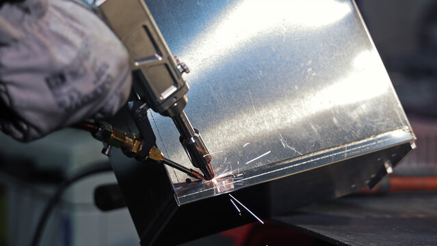Spot welding sheet metal with precision tool. Close-up of a worker using a spot welding machine to fuse sheet metal parts with sparks flying in an industrial setting.