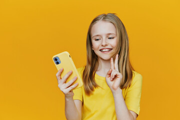 Cheerful young girl with long hair holding a phone, wearing a yellow t shirt, against a vibrant...
