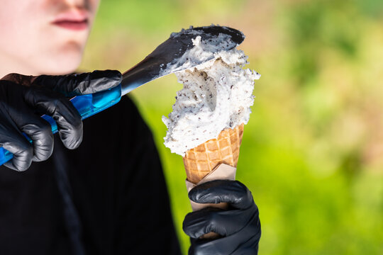 Young girl with gloves preparing a stracciatella flavored ice cream cone with irregular shards of dark chocolate, in a city public park in summer
