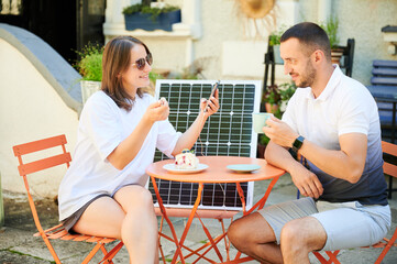 Cute couple relaxing in cafe while woman charging her smartphone. Pretty female using portable...