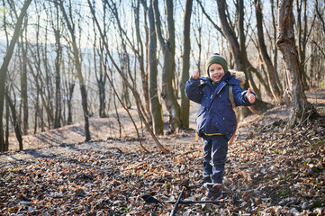 Young child hiking through forest in early spring, warmly dressed in jacket with fur-lined hood,...