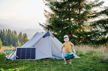 Young child playing near tourist tent with photovoltaic solar panel in summer. On background of...