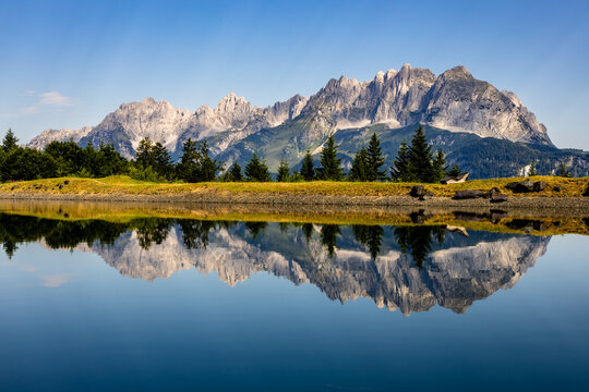 Morning reflection of the Kaisergebirge mountains on the calm surface of Schlosserbergsee lake