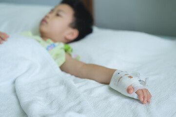 Young child hand with intravenous (IV) line lying in hospital bed, child is receiving medical...