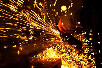 Worker working in industry or factory is holding a cutting stone or grinding stone and sparks are...