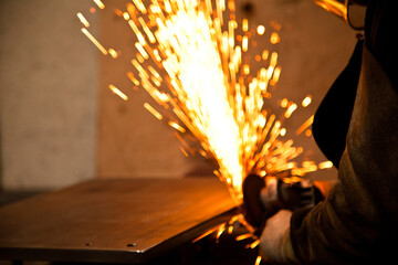 Worker working in industry or factory is holding a cutting stone or grinding stone and sparks are...