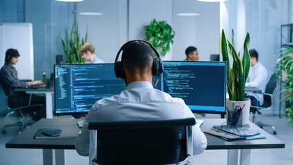A Focused Programmer Working in a Modern Office Environment Surrounded by Colleagues, Monitors Displaying Code and Lush Greenery Enhancing the Workspace