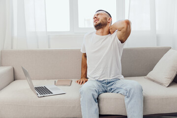 A man experiencing discomfort while working from home, surrounded by technology, highlighting the...