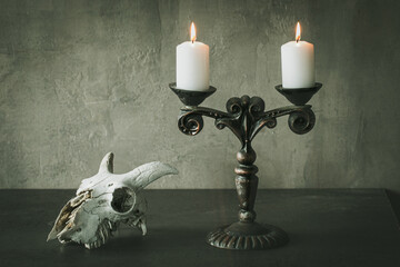 Beautiful vintage metal candelabrum with two burning candles and goats skull on the table, atmospheric image.
