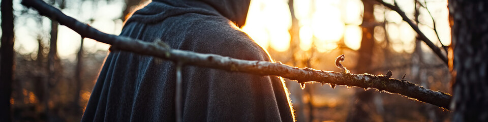 Fototapeta premium Person in Grey Hooded Cloak in Forest at Sunset