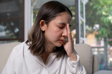 A woman sits on a couch, visibly distressed, with her hand on her forehead, suggesting feelings of...