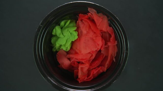 Wasabi and pickled ginger rotates on a black background. Top view