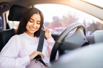 Smiling young Indian woman fastening seatbelt before driving car. Promotes safety, awareness, and...