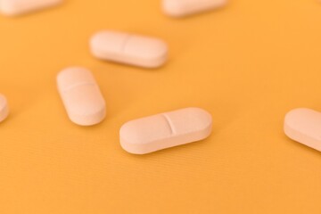 White round pills scattered on a yellow background. Symbol of healthcare, medication, and modern...