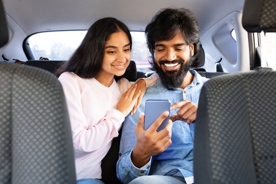 Young smiling indian couple sitting in car backseat, using smartphone together. Shows intimacy, relaxation and digital lifestyle during modern car travel, closeup