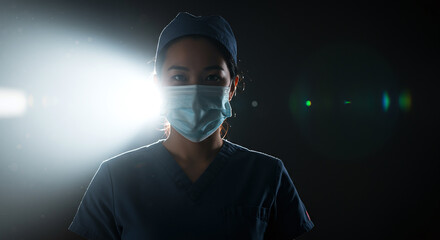 healthcare professional wearing mask and scrubs stands confidently in dramatic light
