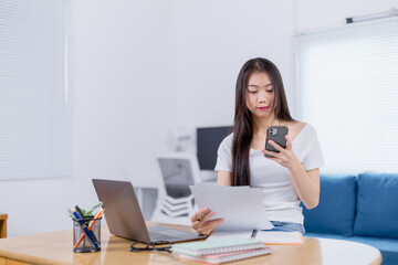 Young asian businesswoman sitting at the desk in the living room working from home managing...