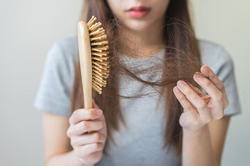 Serious asian young woman holding brush holding comb, hairbrush with fall black hair from scalp...