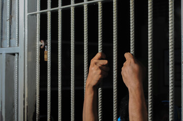 hands of a prisoner behind prison bars on black background