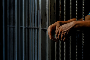hands of a prisoner behind prison bars on black background