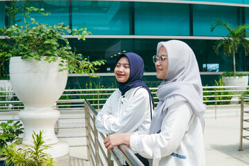 Two Asian women in hijab chatting cheerfully at the airport, enjoying their time together before...