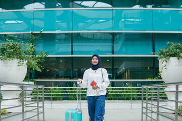 Asian woman in hijab walking through airport corridor, holding her passport and heading confidently...