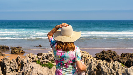 Woman with spaldas with hat on the coast Quebrada full of amazing rock formations, Cantabria, Spain.