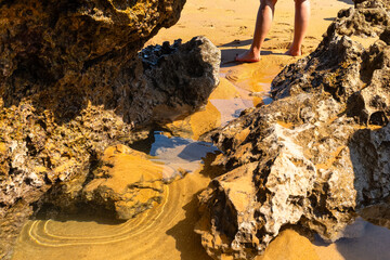 A woman's feet walking among the rocks and sand of the beach of Costa Quebrada, Cantabria, Spain.