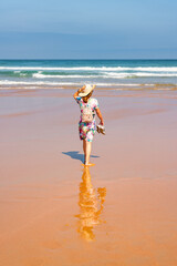 Tourist woman in dress and hat strolling along a lonely golden sand beach in northern Spain, Costa Quebrada, Cantabria.