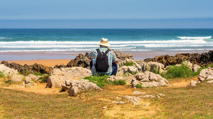 Man with hat sitting with his back to him and enjoying the sea views in northern Spain, Cantabria.