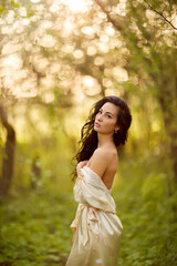 A woman in a white dress stands in an autumn forest. She is naked and hugs herself with her arms.