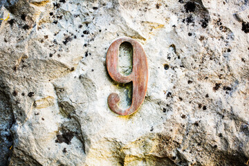 Rustic number 9 mounted on a rugged stone wall. Aged metal texture with natural wear and lichen...
