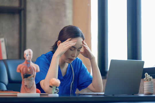 A tired female doctor in blue medical scrubs is working at the hospital.