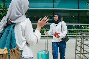 Asian woman in hijab greeting her friend with a warm smile upon arriving at the airport, expressing...