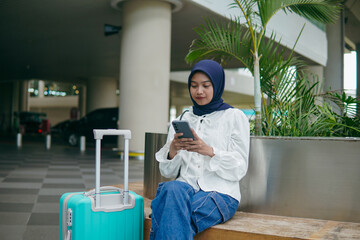 Asian woman in hijab sitting on an airport seat, waiting patiently for her flight and her friend to...