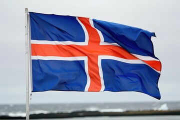 Icelandic flag waving against a cloudy sky near the coastal shoreline during a chilly afternoon