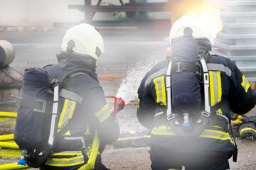 Two firefighters advance together against the flames – equipped with SCBA and a spray nozzle.