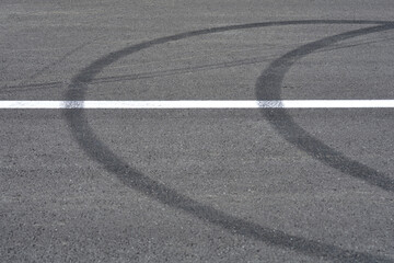 A textured asphalt surface is marked with a bold white line and prominent, dark tire skid marks...