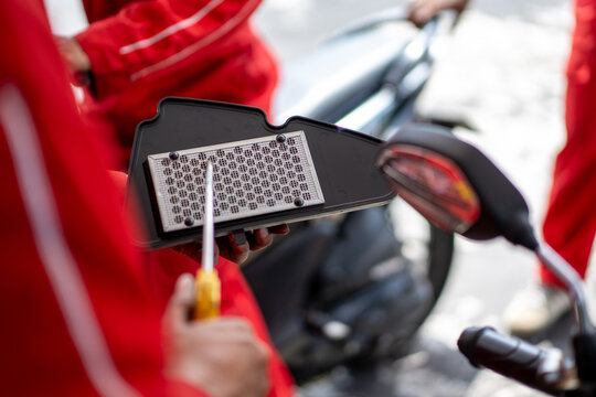 mechanic holding dirty Engine Air Filter over motorcycle and cleaning Filter with air blow gun .mechanic working in motorcycle garage. Repair service and maintenance concept