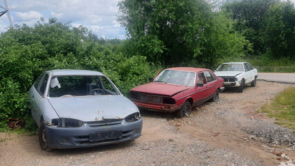 Abandoned rusty cars decaying in junkyard under cloudy sky