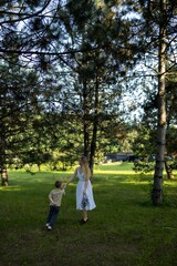 A mother in a white dress walks hand in hand with her child through a bright green forest. They are...