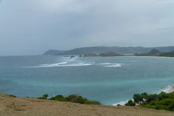 Fototapeten Tropischer Strand Scenic ocean view from Merese Hill in Lombok, Indonesia. Waves crash on rocky islets with turquoise water and lush coastline under a cloudy sky  © Noprian Yosma