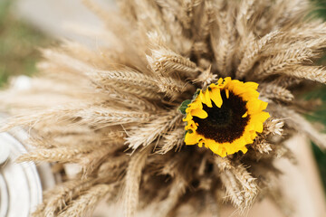 A beautiful mixed bouquet in a rustic style. It is made of ripe grain ears and sunflowers.