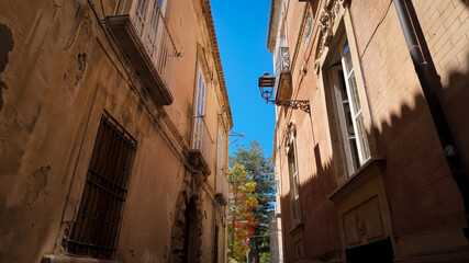 Low angle view of a narrow street with colorful tree and old buildings in Tropea, Calabria, Italy, during a sunny day