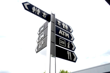 Directional signpost with multiple black arrows and white icons indicating restroom, ATM, tax...