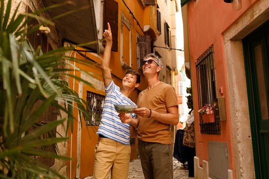 A father and son on a sightseeing trip in Rovinj, Croatia. . They are holding a map. Both appear cheerful and curious, enjoying their time exploring the city together.